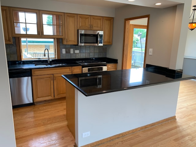 kitchen with appliances with stainless steel finishes, sink, decorative backsplash, and light hardwood / wood-style flooring