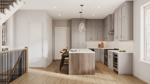 kitchen with gray cabinetry, a center island with sink, decorative light fixtures, light hardwood / wood-style floors, and high end stainless steel range oven