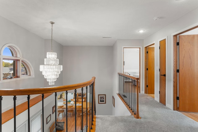 corridor with light colored carpet and a notable chandelier