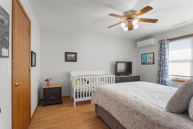 bedroom with an AC wall unit, light wood-type flooring, ceiling fan, and a textured ceiling