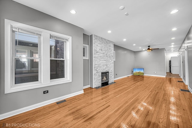 unfurnished living room featuring ceiling fan, a stone fireplace, and light wood-type flooring