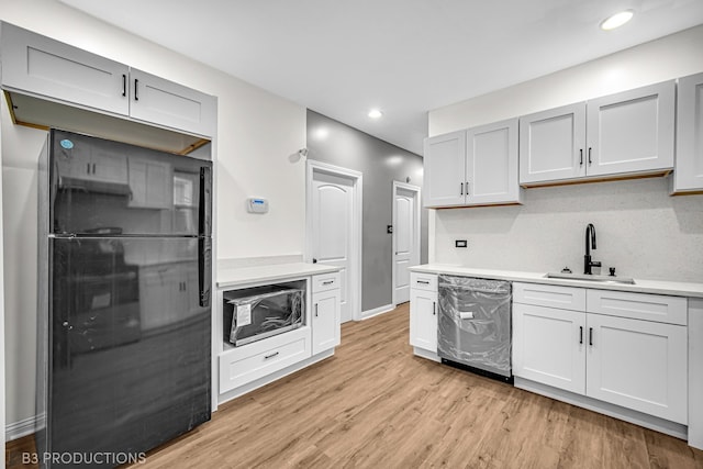 kitchen featuring black fridge, white cabinets, sink, stainless steel dishwasher, and light hardwood / wood-style floors