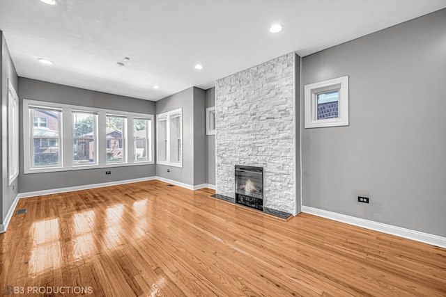 unfurnished living room with light wood-type flooring and a stone fireplace