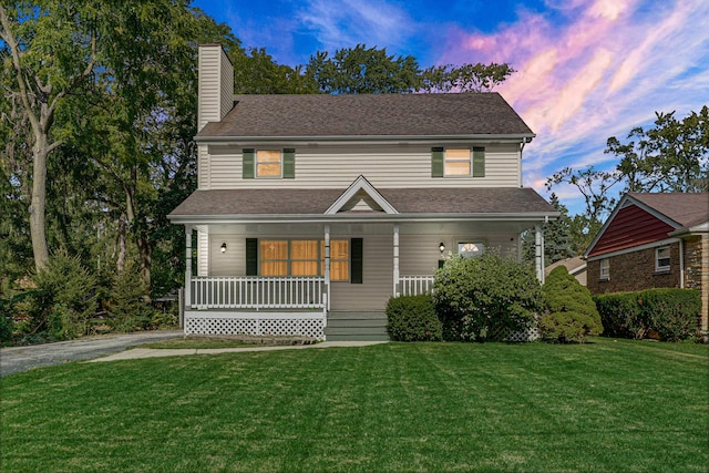 view of front of home featuring roof with shingles, a front lawn, covered porch, and a chimney
