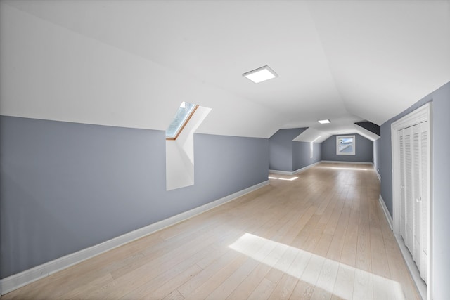 bonus room featuring vaulted ceiling with skylight and light wood-type flooring