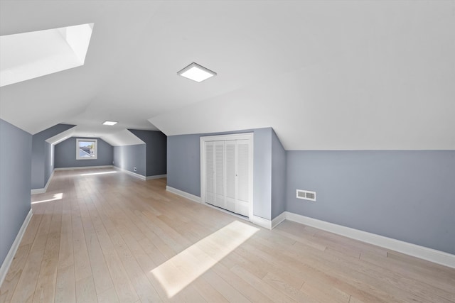 additional living space with light wood-type flooring and vaulted ceiling with skylight