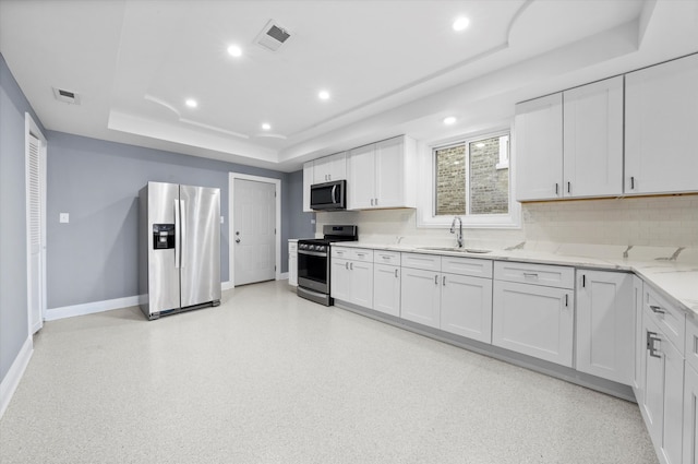 kitchen featuring a raised ceiling, sink, light stone counters, stainless steel appliances, and white cabinets