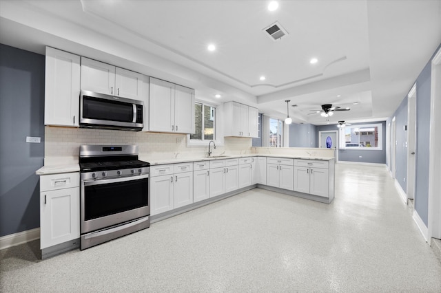 kitchen with a tray ceiling, sink, kitchen peninsula, white cabinets, and appliances with stainless steel finishes