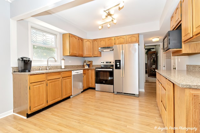 kitchen featuring appliances with stainless steel finishes, light wood-type flooring, light stone countertops, and sink