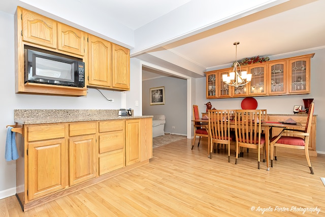 kitchen with light wood-type flooring, light stone counters, a notable chandelier, ornamental molding, and decorative light fixtures