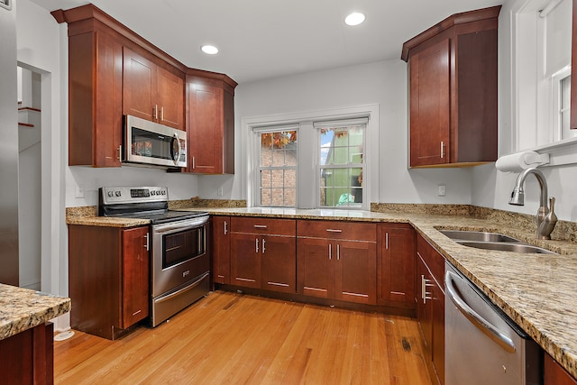 kitchen with sink, light stone countertops, stainless steel appliances, and light hardwood / wood-style flooring