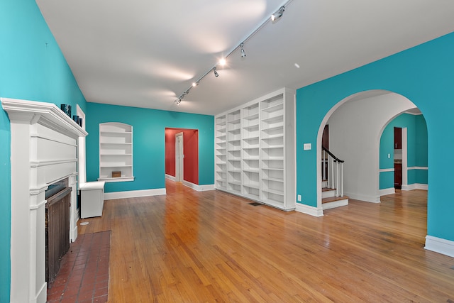 unfurnished living room featuring built in shelves, hardwood / wood-style floors, and track lighting