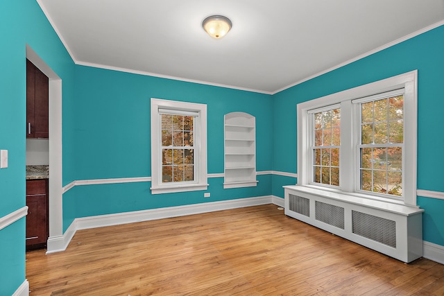 unfurnished room featuring built in features, light wood-type flooring, radiator heating unit, and crown molding