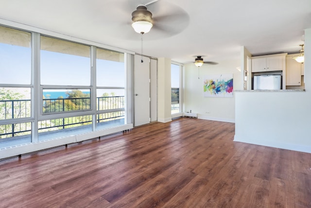 unfurnished living room featuring dark wood-type flooring, ceiling fan, and a wealth of natural light