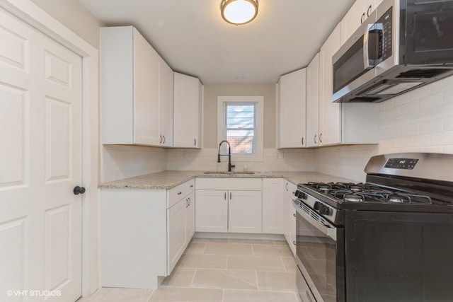 kitchen with light stone counters, stainless steel appliances, white cabinets, sink, and light tile patterned floors