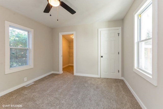 unfurnished bedroom featuring light carpet, a walk in closet, and ceiling fan