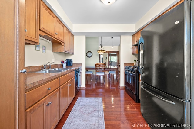 kitchen with pendant lighting, dark wood-type flooring, black appliances, and sink