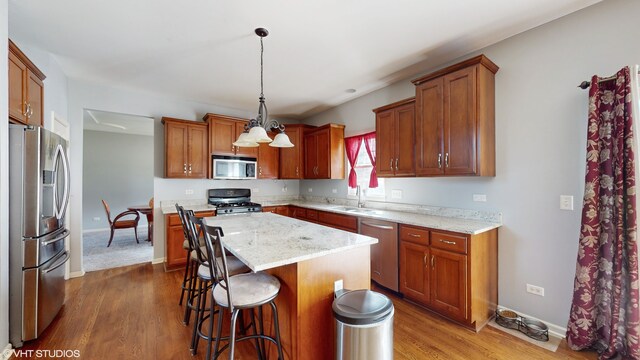 kitchen featuring light stone countertops, stainless steel appliances, hardwood / wood-style floors, a kitchen island, and hanging light fixtures