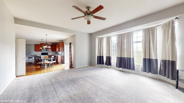 unfurnished living room featuring dark carpet, ceiling fan, and a healthy amount of sunlight