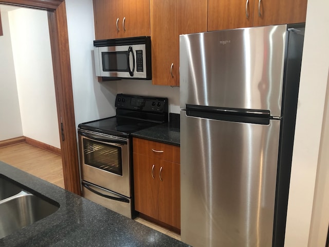 kitchen with appliances with stainless steel finishes, dark stone counters, and light wood-type flooring