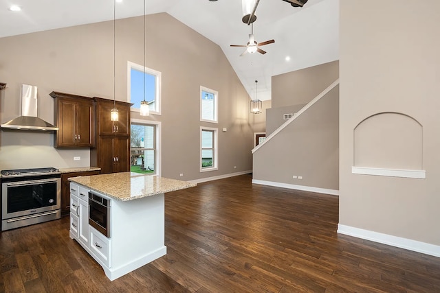 kitchen featuring decorative light fixtures, wall chimney range hood, high vaulted ceiling, appliances with stainless steel finishes, and dark hardwood / wood-style floors