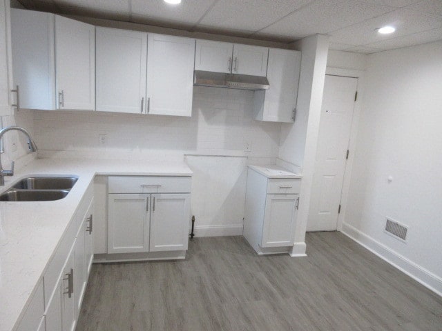 kitchen with decorative backsplash, white cabinets, a drop ceiling, sink, and light hardwood / wood-style flooring