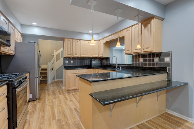 kitchen featuring light hardwood / wood-style floors, kitchen peninsula, dark stone counters, hanging light fixtures, and appliances with stainless steel finishes