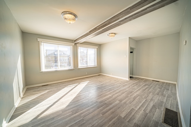 empty room featuring beamed ceiling and light hardwood / wood-style flooring