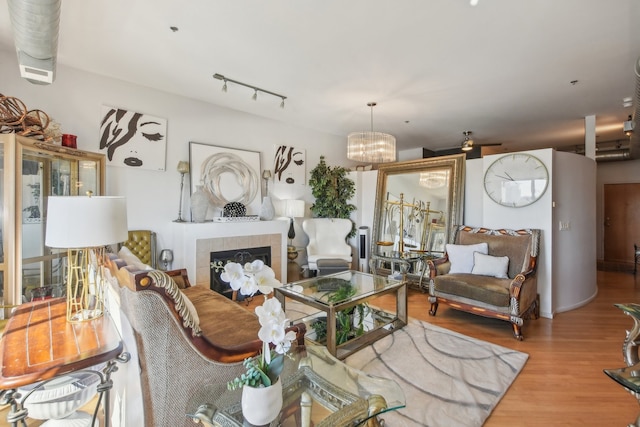 living room featuring a fireplace, rail lighting, a chandelier, and light hardwood / wood-style flooring