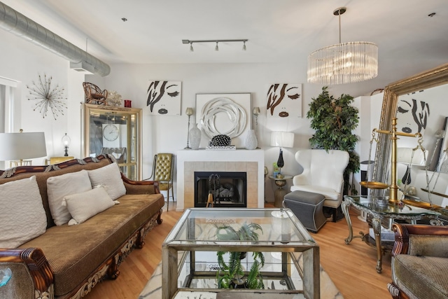 living room featuring wood-type flooring, a notable chandelier, rail lighting, and a tile fireplace