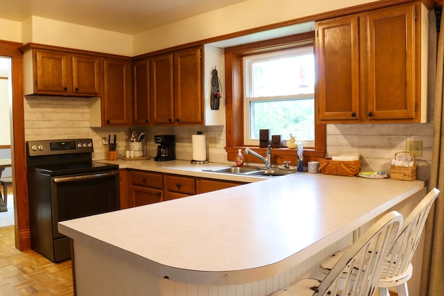 kitchen featuring light parquet floors, sink, black electric range, kitchen peninsula, and a kitchen bar