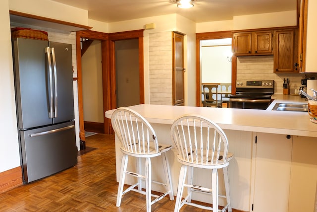 kitchen with appliances with stainless steel finishes, parquet flooring, a kitchen bar, and decorative backsplash