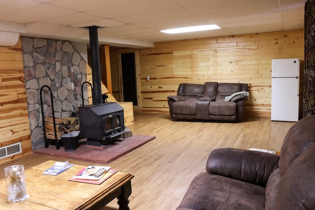 living room featuring a wood stove, a drop ceiling, wood walls, and light hardwood / wood-style floors