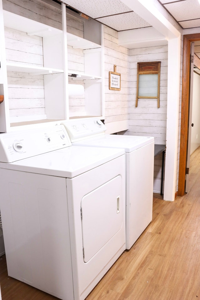 clothes washing area with light wood-type flooring, washer and dryer, and wooden walls