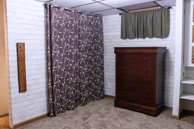 bedroom featuring light carpet, a paneled ceiling, and wood walls