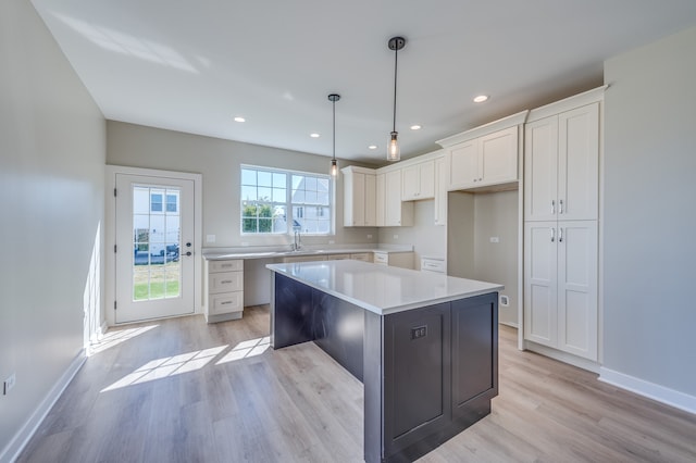 kitchen featuring white cabinets, sink, a kitchen island, decorative light fixtures, and light wood-type flooring