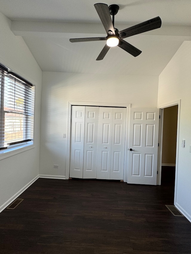 unfurnished bedroom with ceiling fan, a closet, dark hardwood / wood-style floors, and vaulted ceiling with beams