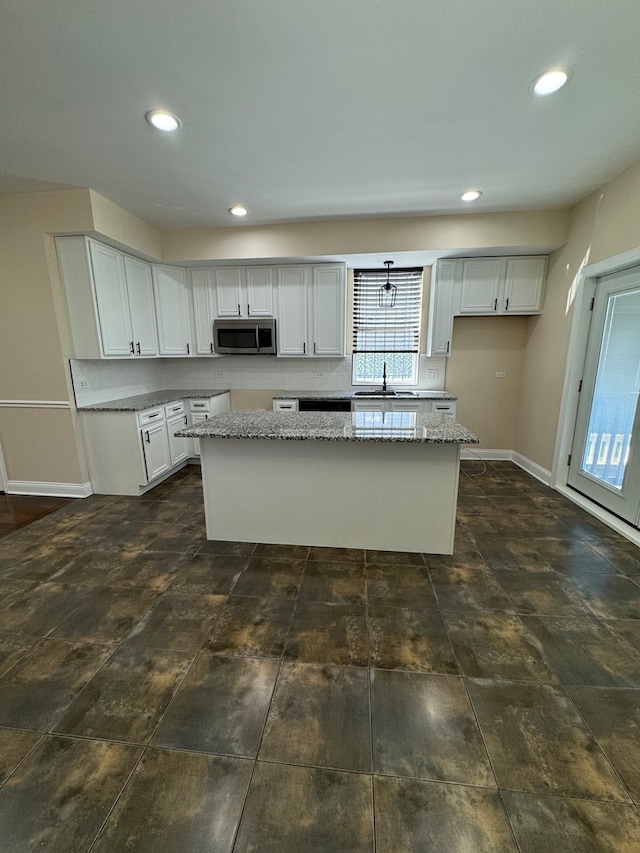 kitchen with light stone countertops, a center island, sink, and white cabinets