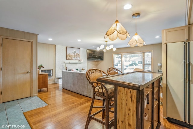 kitchen with stainless steel refrigerator, light wood-type flooring, a breakfast bar area, light brown cabinets, and hanging light fixtures