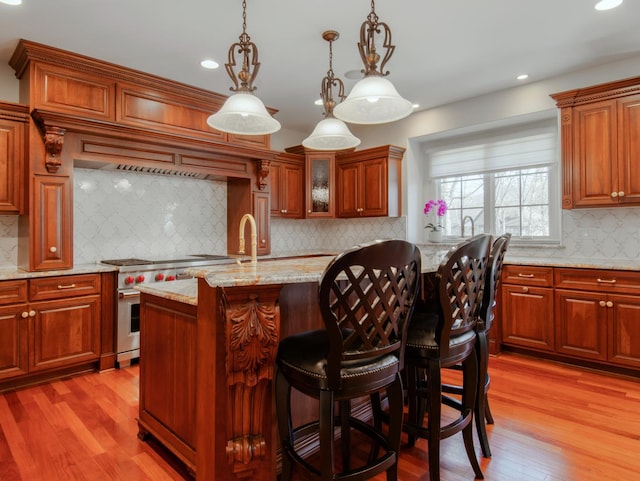 kitchen with stainless steel stove, a breakfast bar, hanging light fixtures, light stone counters, and light wood-type flooring