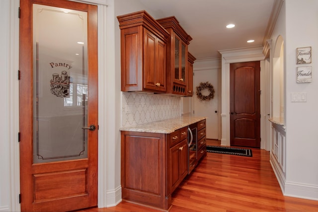 kitchen featuring crown molding, backsplash, light stone counters, and light hardwood / wood-style flooring