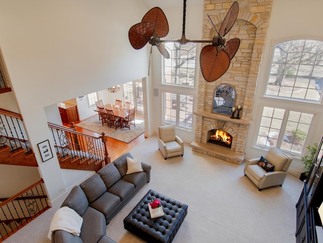 carpeted living room with a stone fireplace, a wealth of natural light, and a high ceiling