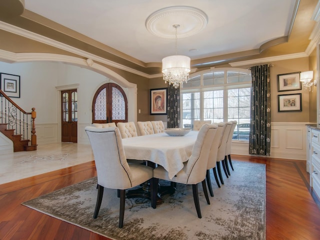 dining area featuring french doors, crown molding, a tray ceiling, a notable chandelier, and hardwood / wood-style flooring