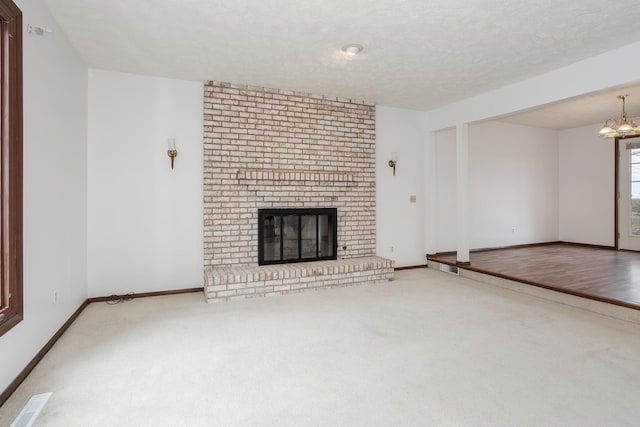 unfurnished living room with a textured ceiling, carpet floors, a fireplace, and an inviting chandelier