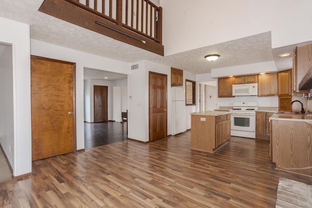 kitchen with dark hardwood / wood-style flooring, white appliances, a kitchen island, and sink