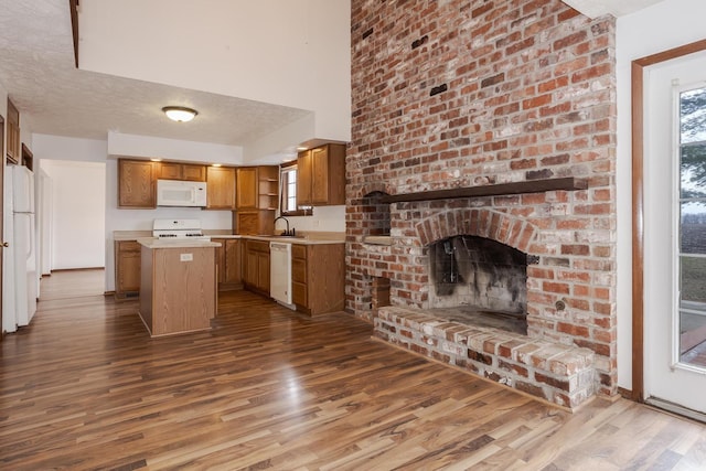 kitchen featuring a brick fireplace, white appliances, a textured ceiling, hardwood / wood-style flooring, and a kitchen island