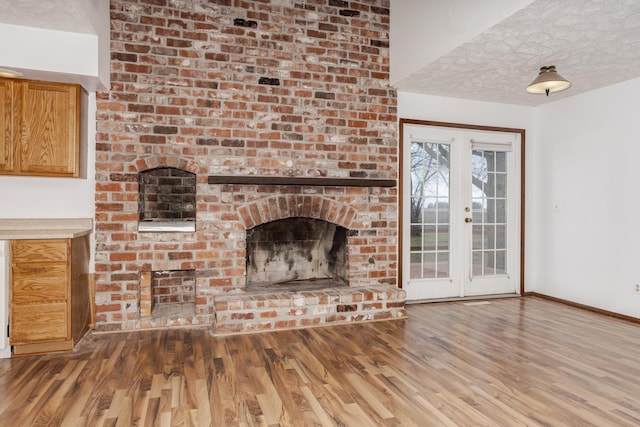 unfurnished living room with a textured ceiling, a fireplace, hardwood / wood-style flooring, and french doors