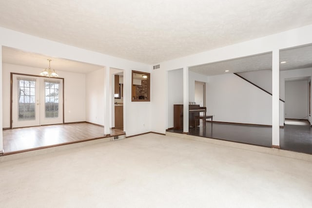 unfurnished living room featuring carpet flooring, french doors, a textured ceiling, and a notable chandelier