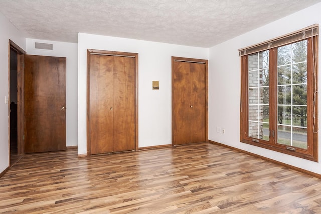 unfurnished bedroom with light wood-type flooring, a textured ceiling, and multiple closets