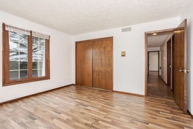 unfurnished bedroom featuring a textured ceiling, light hardwood / wood-style floors, and a closet